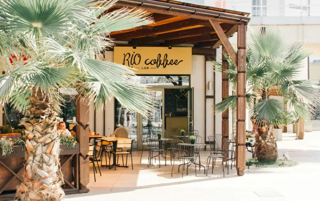 An inviting outdoor café under palm trees with wooden tables and chairs on a sunny day.